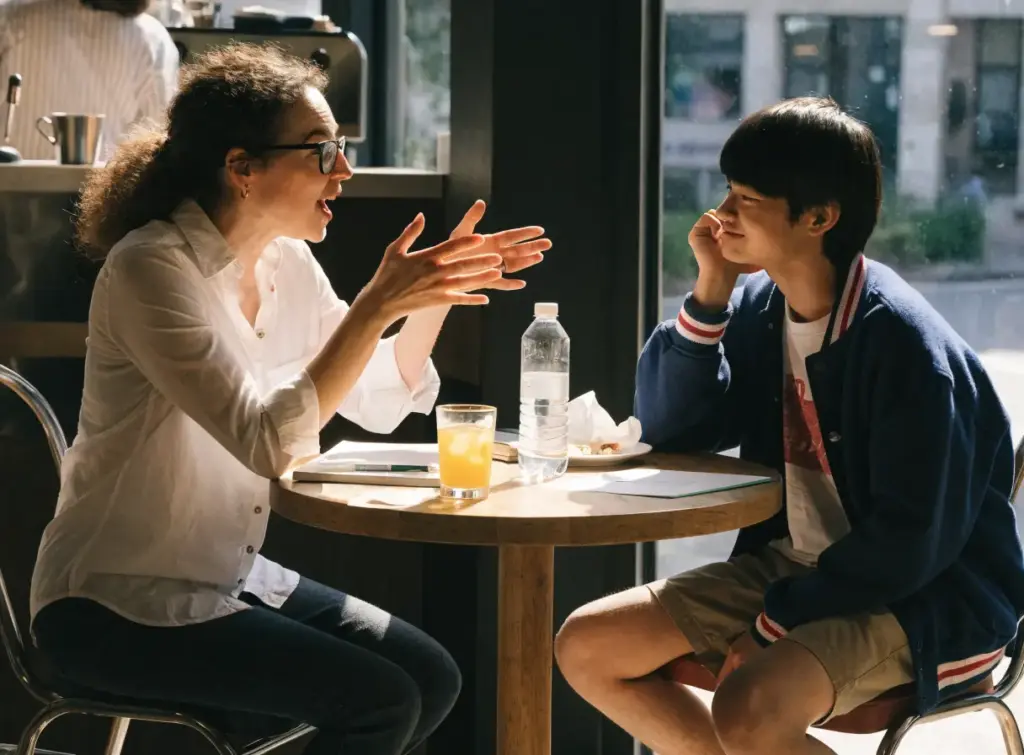 Two people in conversation at a cafe table, speaking examiner evaluation